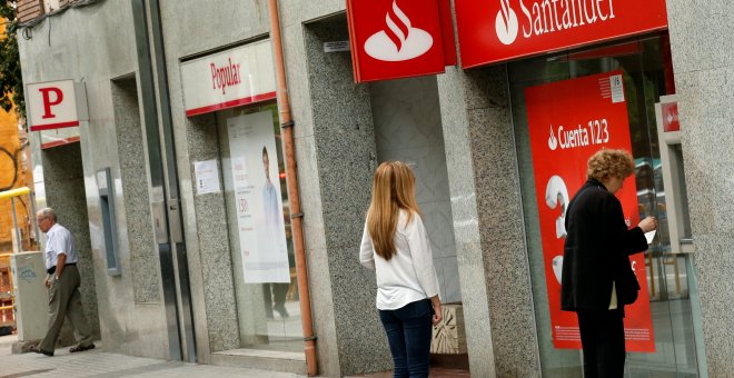 Un par de personas utilizan un cajero automático de una oficina del Banco Santander, en Barcelona, situada junto a una sucursal del Popular. REUTERS/Albert Gea