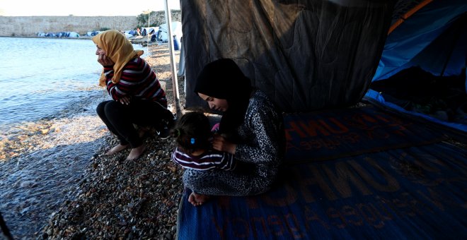 Faten (i), procedente de Siria, se sienta a la orilla del mar junto a su nuera, cerca de su tienda en el campo de refugiados de Souda, en la isla de Chios. "Está tardando demasiado. Esta lentitud para traer a toda la familia me asusta", dice Faten. "No te