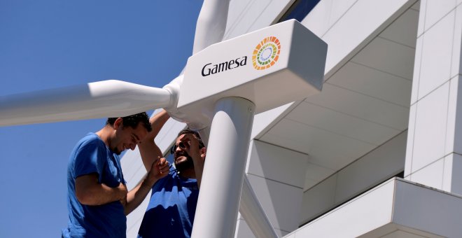 Dos operarios con la maqueta de un aerogenerador en la entrada de la sede de Gamesa, en Zamudio. REUTERS